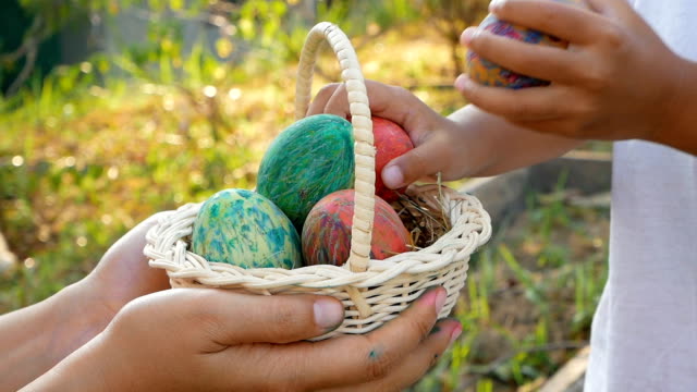 Close-up-of-woman-hand-holding-a-basket-with-easter-eggs.-Children-put-eggs-into-basket-in-sunshine-background
