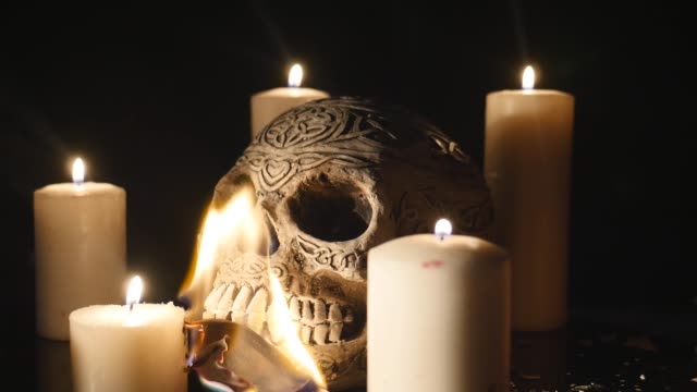 Brennende-Dollar-mit-vier-brennenden-Kerzen-und-einem-Totenkopf-hautnah-auf-schwarzem-Hintergrund