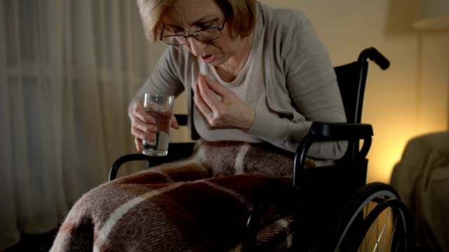 Alte-Frau-im-Rollstuhl-Einnahme-Pille-mit-zitternden-Händen,-trauriges-Leben-im-Pflegeheim