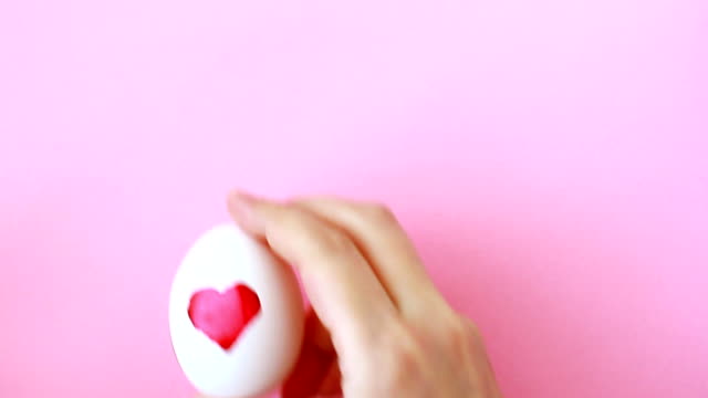 Female-hand-puts-egg-with-painted-watercolor-heart-for-Easter-on-pink-background