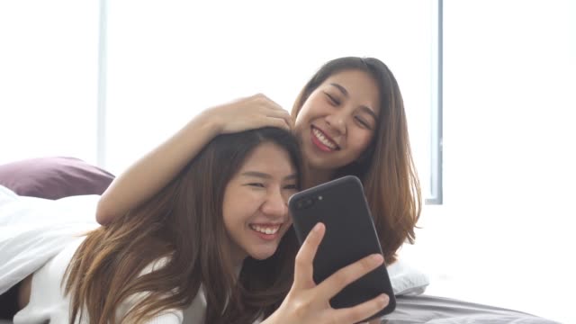 Slow-Motion---schöne-junge-asiatische-Frauen-LGBT-lesbische-glückliche-Paar-sitzt-am-Bett-Umarmung-und-Telefon-unter-Selfie-zusammen-Schlafzimmer-zu-Hause-benutzen.-LGBT-lesbisches-Paar-gemeinsam-im-Haus-Konzept.