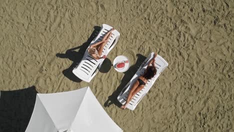Aerial:-young-beautiful-model-girls-lie-on-lounges,-posing-in-designer-bikini