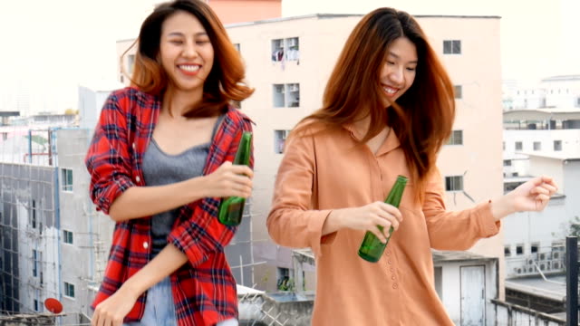 Mujer-asiática-joven-pareja-de-lesbianas-bailando-y-tintineantes-botellas-de-cerveza-fiesta-en-la-azotea.