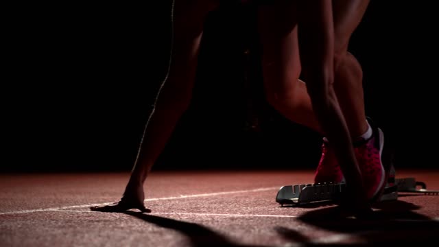 Tres-deportes-a-los-atletas-de-la-chica-por-la-noche-en-el-comienzo-de-la-cinta-de-correr-para-la-carrera-en-la-distancia-sprint-desde-la-posición-sentada