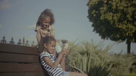Fröhliche-Kinder-mit-Ihrem-Smartphone-auf-Bank-sitzend