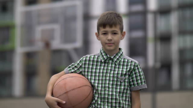 Bildnis-eines-Knaben-mit-einem-Basketball-Ball-auf-einem-Basketballfeld,-befasst-sich-mit-der-Kamera
