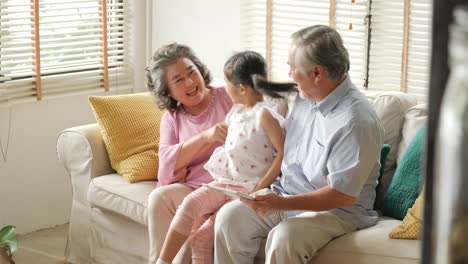 Niña-viene-a-abrazar-a-su-abuelo-y-su-abuelo-mientras-jugar-tablet.-Niño-jugando-con-senior-hombre-y-mujer-feliz-emoción.-personas-con-familia,-estilo-de-vida,-concepto-de-tecnología.