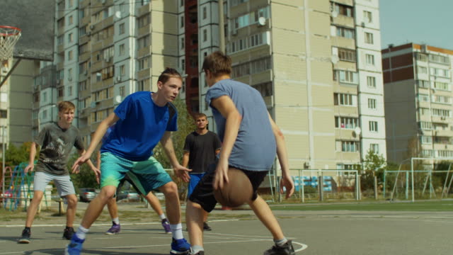 Teenage-streetball-player-dribbling-and-bouncing-the-ball-on-the-floor,-passing-to-his-teammate-while-playing-basketball-game-on-street.-Basketball-guard-stealing-a-ball-and-running-in-fast-break.