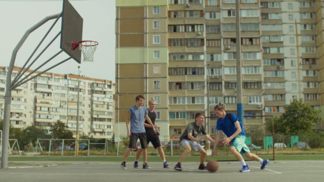 Teenager-Freunde-spielen-Streetball-auf-Freiplatz