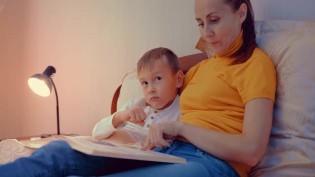 Cute-toddler-boy-reading-book-with-mother-before-going-to-sleep