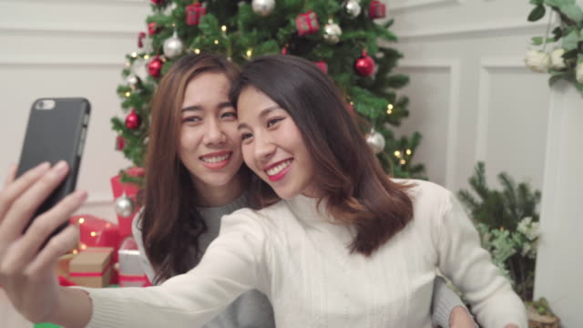 Group-of-cheerful-happy-young-Asian-woman-using-smartphone-selfie-with-christmas-tree-decorate-her-living-room-at-home-in-Christmas-Festival.-Lifestyle-women-celebrate-Christmas-and-New-year-concept.