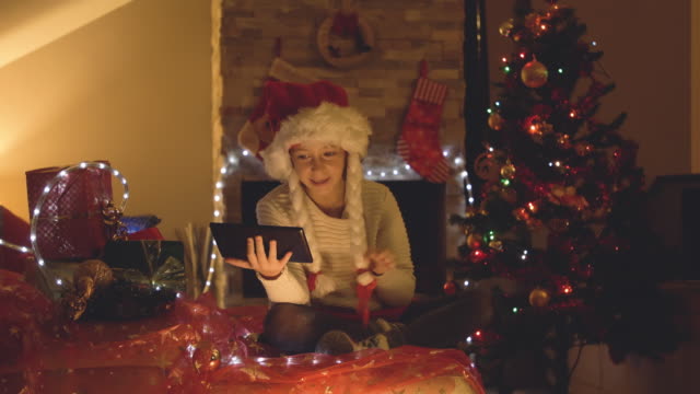 Happy-little-girl-using-tablet-on-a-video-call-at-Christmas-in-decorated-living-room-with-tree-and-chimney.