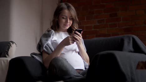 Mujer-embarazada-con-teléfono-móvil-en-la-silla-del-brazo
