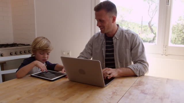 Padre-e-hijo-usando-computadoras-en-la-mesa-de-la-cocina,-filmado-en-R3D