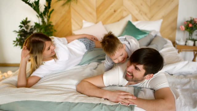Eine-junge-Familie-mit-kleinem-Sohn-spielen-auf-dem-Bett-im-Schlafzimmer