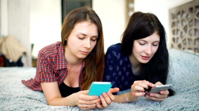 Dos-felices-amigas-compartir-las-redes-sociales-en-un-teléfono-inteligente-y-hablar