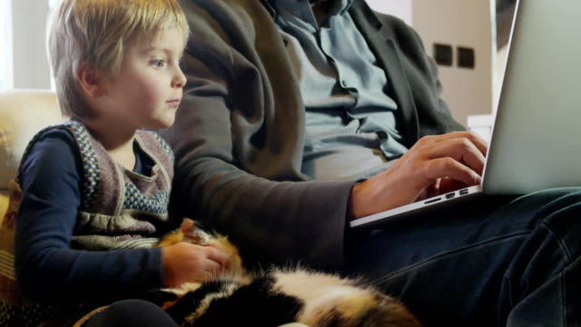 moderne-Familie-kleines-Mädchen-spielt-mit-Katze-während-Papa-arbeitet-mit-Notebook-auf-Couch-indoor-in-modernen-industriellen-Haus.-Kaukasische.-4k-handheld-nahaufnahme-Slow-Motion-video-gedreht
