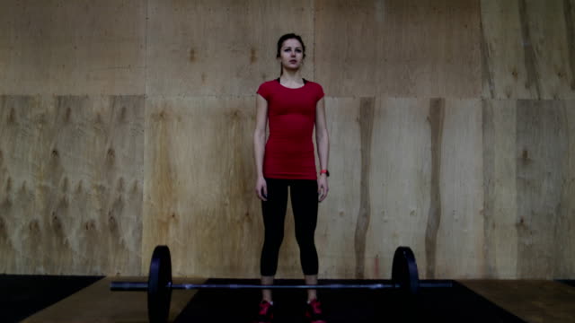 Athletic-Woman-Athlete-Portrait-Standing-In-Front-Of-Weights-Before-Lifting-In-Center
