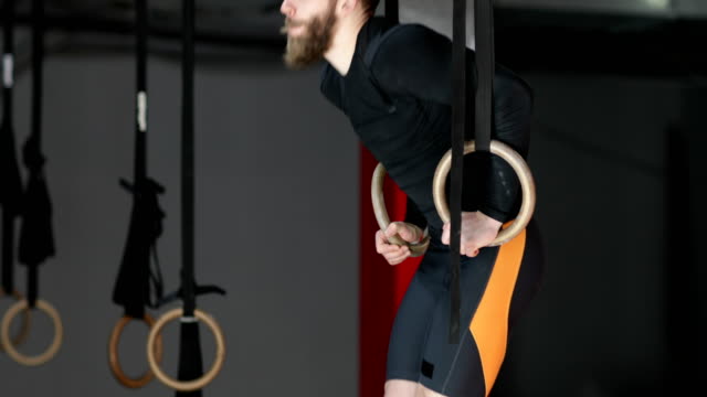 Young-Man-Exercising-On-Gymnastic-Rings-During-Workout-Training-At-Gym