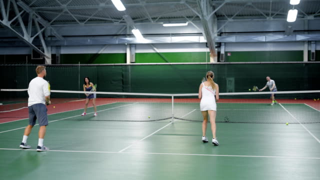 Eine-Gesellschaft-von-Freunden-Tennis-spielen-auf-dem-Sportplatz,-Erwachsene-Männer-und-Frauen-werfen-einen-Tennisball-auf-verschiedenen-Seiten-des-Feldes