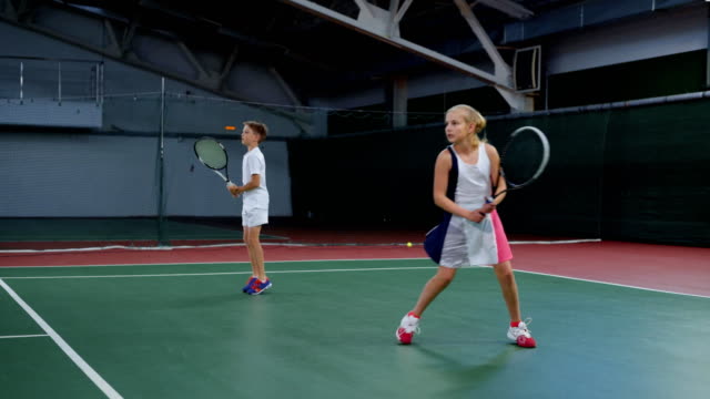 Deportivo-niño-y-niña-practicando-con-raquetas-de-tenis-en-cancha-de