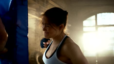 Sportliche-Frau-Hits-Boxsack,-ihrem-Lebensgefährten-/-Trainer-hält.-Sie-ist-professionelle-Kämpfer-und-Training-in-einem-Fitnessstudio.