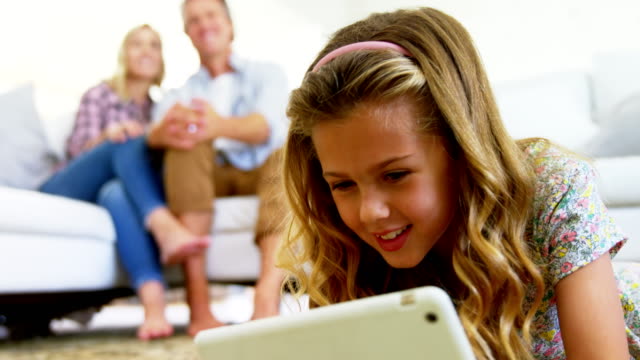 Hija-con-tableta-digital-en-la-sala-mientras-los-padres-sentados-en-el-sofá-4k