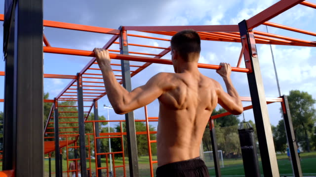 Back-side-view-of-young-topless-sportsman-chin-ups.-Sports-field-in-background.