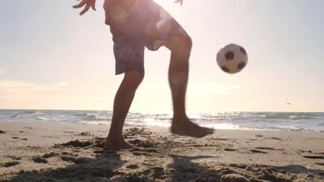 Young-man-in-swimming-trunks-doing-tricks-holding-football-on-the-foot-on-the-sea-shore-at-the-beach-at-sunset-silhouette