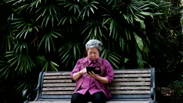 Asia-mujer-mayor-sosteniendo-el-teléfono-móvil-en-el-jardín.-mensaje-de-texto-mujeres-mayores,-con-la-aplicación-de-teléfono-inteligente-en-el-parque.-teléfono-móvil-de-uso-principal-para-conectar-con-la-red-social