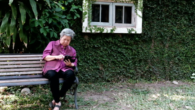 Asia-mujer-mayor-sosteniendo-el-teléfono-móvil-en-el-jardín.-mensaje-de-texto-mujeres-mayores,-con-la-aplicación-de-teléfono-inteligente-en-el-parque.-teléfono-móvil-de-uso-principal-para-conectar-con-la-red-social