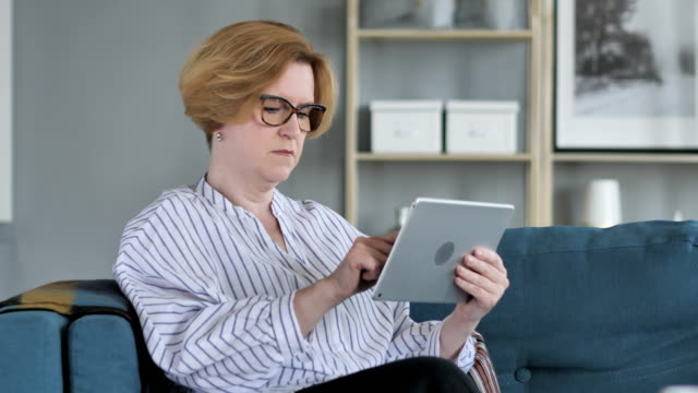 Old-Senior-Woman-Browsing-Internet-on-Tablet-PC,-Sitting-on-Couch
