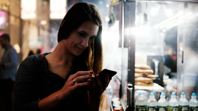 Glücklich-attraktiven-weiblichen-CEO-mit-Smartphone-e-Commerce-app-in-der-Nähe-von-dampfenden-Suppen-Hersteller-in-New-York-City-am-Abend