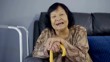 senior-woman-laughing-and-holding-wooden-cane-in-living-room-at-home