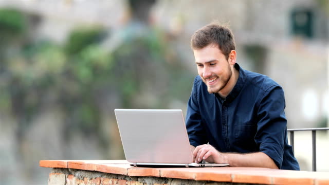 Hombre-feliz-escribiendo-en-un-ordenador-portátil-en-un-balcón
