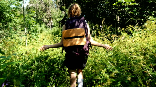 Touristen-Frau-mit-einem-Rucksack-zu-Fuß-in-ein-Feld-von-Wildblumen-in-einem-Nationalpark-in-den-Wald-im-Sommer.-Mädchen-berührt-den-Rasen