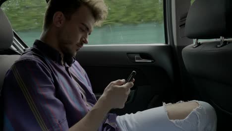 Hombre-joven-que-viaja-en-coche-en-la-ciudad-viendo-pasar-app-en-pantalla-táctil-ver-contenido-divertido-en-la-pantalla-del-smartphone-durante-el-recorrido