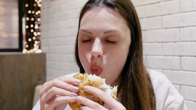 Woman-eating-a-hamburger-with-relish-and-delight-in-cafe.