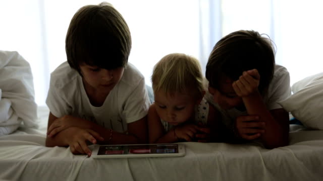 Brothers,-playing-in-bed-on-tablet,-enjoying-their-summer-holiday