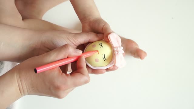 Women's-and-children's-hands-hold-chicken-egg-decorated-for-Easter-chick,-draw-chicken-muzzle-with-marker.