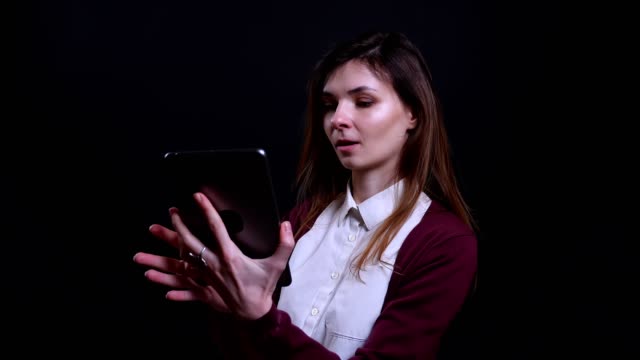 Portrait-of-young-brunette-businesswoman-making-beautiful-selfie-photos-on-tablet-happily-on-black-background.