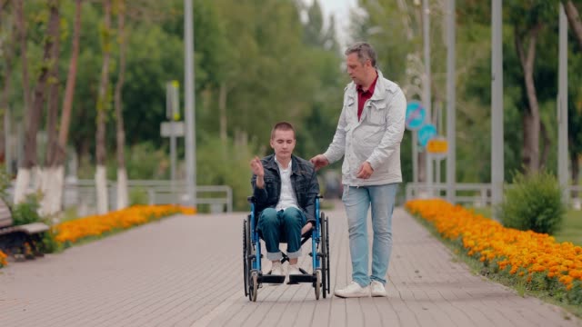 Young-man-gets-up-from-the-wheelchair-and-walks-over.-Father-helps-his-son-get-up-from-the-wheelchair-and-walk.