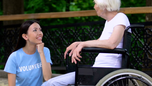 Freiwilliges-Gespräch-mit-behinderter-alter-Dame-im-Rollstuhl-im-Pflegeheimpark