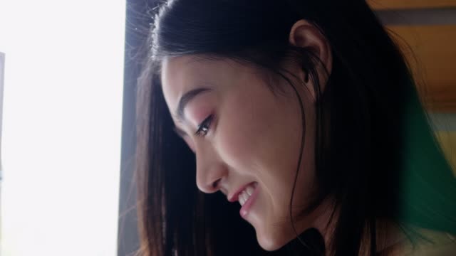 Close-up-a-smiling-portrait-of-a-beautiful-caucasian-Asian-woman-using-smartphone-shopping-online-and-use-the-credit-card-payment-while-standing-beside-the-window-at-the-office-room.