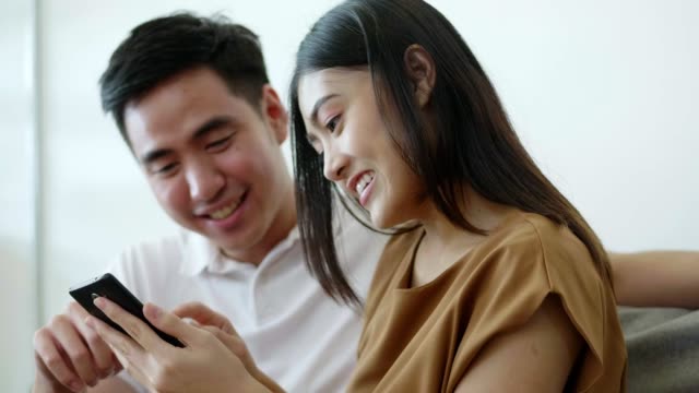 Slow-Motion:-Cierra-a-la-pareja-asiática-usando-la-comunicación-de-redes-sociales-y-comprando-en-línea-mientras-estás-sentado-en-el-sofá-en-casa.