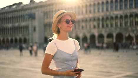 Joven-caucásica-turista-con-vestido-azul-caminando-en-la-plaza-en-Roma-revisando-el-correo-de-un-amigo-en-el-teléfono-inteligente-conectado-a-4G-en-itinerancia