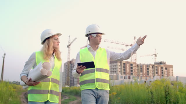 Engineer-and-controller-go-to-the-construction-site-on-the-background-of-cranes-and-talk-about-work.-Discussion-with-the-contractor-on-the-construction-progress
