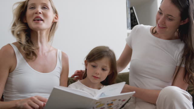 Gleich-Geschlecht-weibliche-paar-lesen-Buch-mit-Tochter-zu-Hause-zusammen