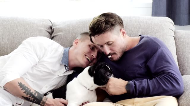 Gay-couple-relaxing-on-couch-with-dog.-Enjoy-feeding-a-dog-by-mouth.