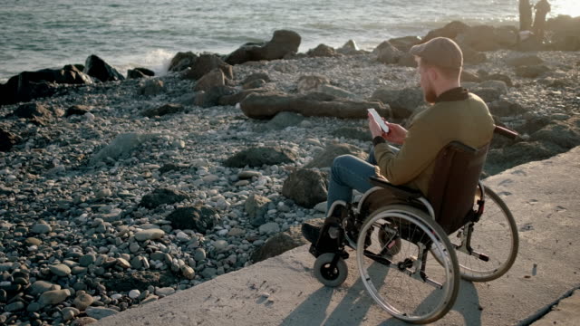 Behinderter-Mann-Surfnetz-auf-dem-Handy-beim-Entspannen-am-Meer